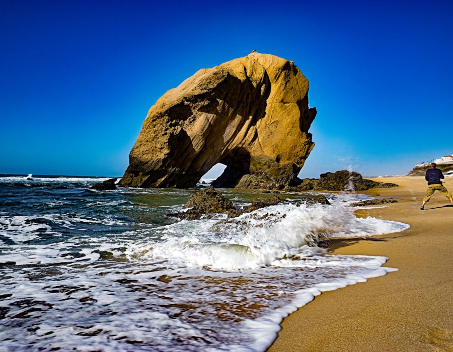 Strand am Penedo do Guincho mit einem Fotografen, der vor einer Welle wegrennt