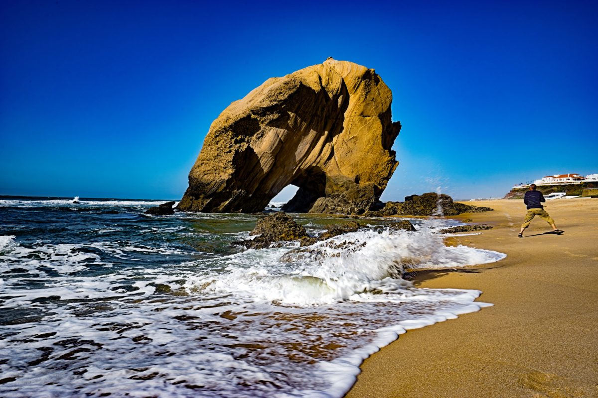Strand am Penedo do Guincho mit einem Fotografen, der vor einer Welle wegrennt